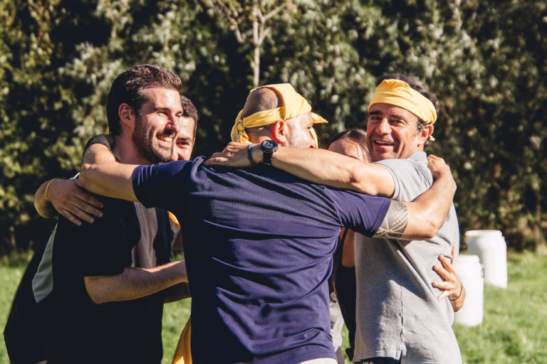 Collega's omhelzen elkaar lachend tijdens een teamuitje in de buitenlucht