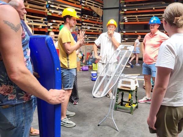 Medewerkers met bouwhelmen bouwen een kettingreactie in de hal van Almetaal tijdens het 30-jarig jubileum